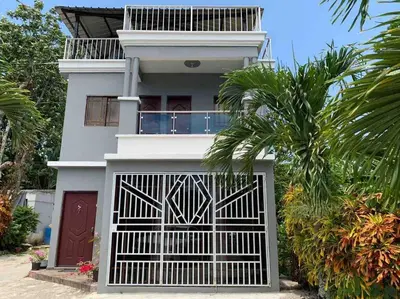 a white house with a gate and a palm tree at Casa Linda - 10 mins from Beach & Lagoon with AC & Free Parking in Payita