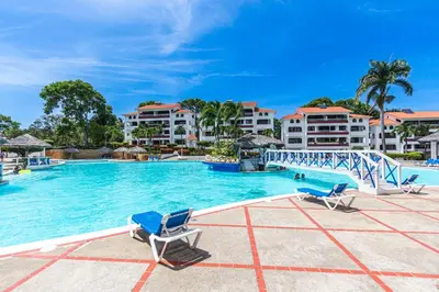 a pool at a resort with two chairs and a bridge at Monte Vista Apartments in Sosúa