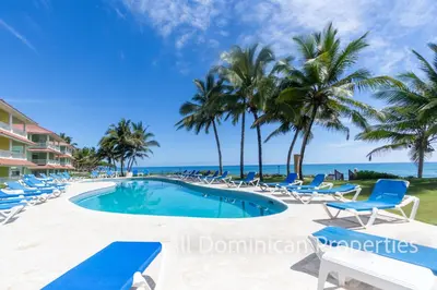 a resort pool with chairs and palm trees on the beach at Victorian Condominium, Cabarete! in Cabarete