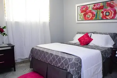 a bedroom with a bed with white sheets and red pillows at Apartamento entero en Samaná Los tios 1 y 2 in Santa Bárbara de Samaná