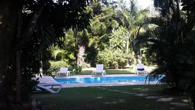 three lounge chairs and a swimming pool in a yard at Bungalow Natura Village in Sosúa