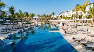 a pool at a resort with lounge chairs and palm trees at Secrets Tides Punta Cana - All Inclusive in Punta Cana
