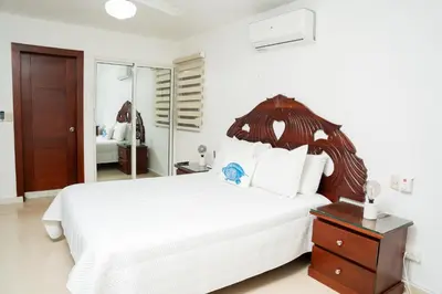 a bedroom with a large white bed with a wooden headboard at Apartamento Los Anturios en Puerto Plata Bayardo in San Felipe de Puerto Plata