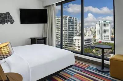 a hotel room with a white bed and a large window at Aloft Santo Domingo Piantini in Santo Domingo
