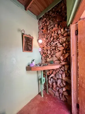 a bathroom with a stone wall with a wooden sink at La Hacienda Hostel-Rancho in Las Galeras