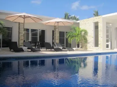a pool with chairs and umbrellas next to a house at Villa Palmas Doradas in Cabarete