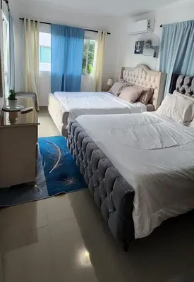 two beds in a bedroom with blue curtains and a table at Rooftop with Pool, La Romana, Villa Doña Julia, At Paula Isabel in La Romana