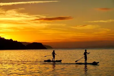 two people are paddleboarding on the water at sunset at Las Terrenas Villa- King Bed, Beaches & Dining in Las Terrenas