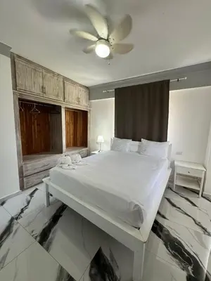 a bedroom with a white bed with a ceiling fan at Las Palmeras by Graziano in Boca Chica