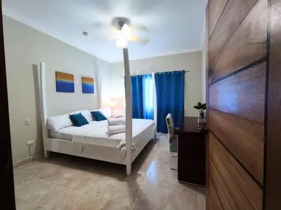 a bedroom with a bed with blue curtains and a table at BeachFront Apartament - Private Beach Access in Punta Cana