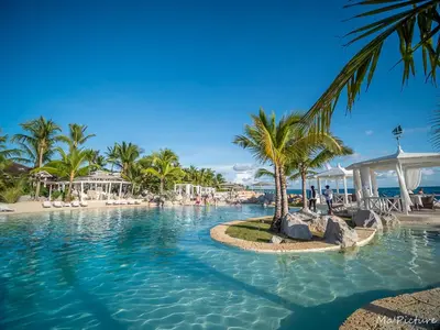 a resort swimming pool with palm trees and a beach at TRACADERO Beach Club & Holidays Rentals in Bayahibe