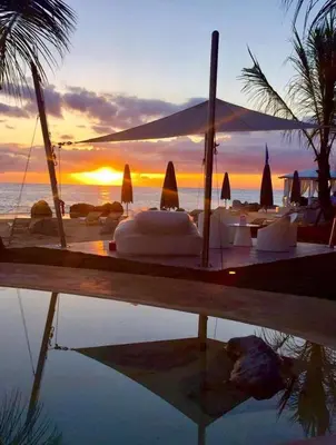 a sunset over a beach with tables and umbrellas at TRACADERO Beach Club & Holidays Rentals in Bayahibe
