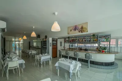 a restaurant with white tables and chairs and a bar at Hotel Plaza Europa in Sosúa