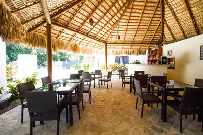 a restaurant with tables and chairs under a straw umbrella at Coral Blanco Hotel in Sosúa