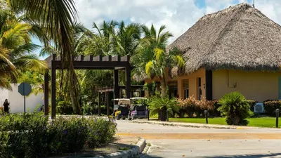 a building with a thatched roof and palm trees at Comfort Condo w/Pool View at Hard Rock Golf Course in Punta Cana