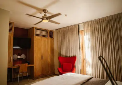 a bedroom with a red chair and a ceiling fan at Billini Hotel, Historic Luxury in Santo Domingo