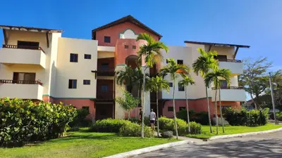 a man standing in front of a building with palm trees at Apartamentos Essential Life con playa y piscina in Punta Cana
