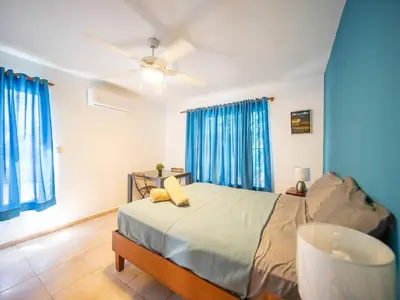 a bedroom with a bed with blue curtains and a ceiling fan at 2br Caribbean Condo In Cabarete Center in Cabarete