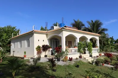 a white house with palm trees in a yard at CasaMia RD B&B in Río San Juan