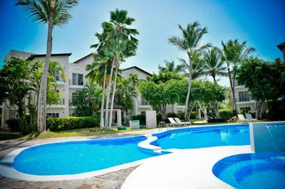 a swimming pool in front of a building with palm trees at White Sands Punta Cana - Pool-Jacuzzi in Punta Cana