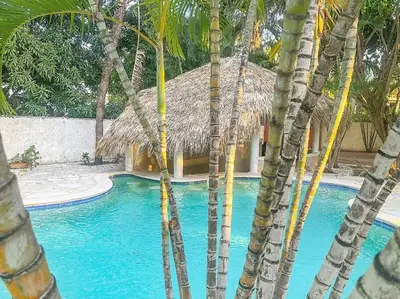 a swimming pool with palm trees in front of a building at Villa Infinito Bani's Exclusive Beachside Mansion in Baní