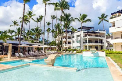 a swimming pool in front of a building with palm trees at Aligio Apart-hotel & Spa - Las Terrenas in Las Terrenas