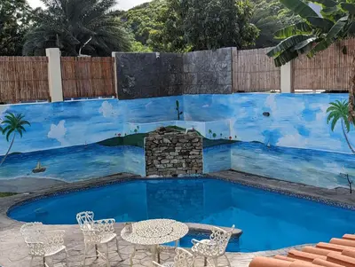 a pool with tables and chairs in front of a blue wall at 1BR Suite at Villa Costa Verde near Playa Cofresi, Puerto Plata, with a pool, balcony and a rooftop terrace in San Felipe de Puerto Plata