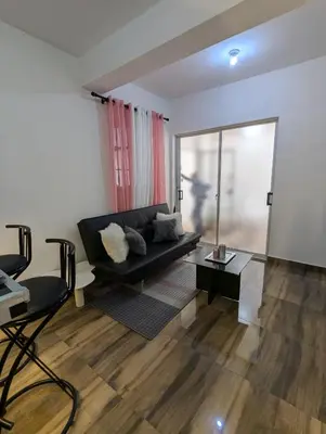 a living room with a black couch and a large window at A 7 minutos del Aeropuerto SDQ, Moderno y Compacto Apartamento in Boca Chica