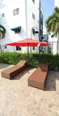 two benches and a red umbrella in front of a building at Harmony II , 5 Min to Airport, Pool View Balcony in Santiago de los Caballeros