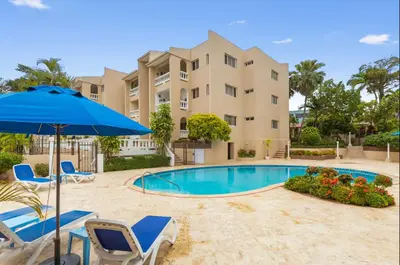 a swimming pool with chairs and an umbrella and a building at El Neptuno Residencial, Sosua in Sosúa