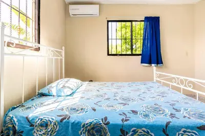 a bedroom with a bed with a blue comforter and a window at Casa para vacacionar - El patio de Olivia in San Felipe de Puerto Plata