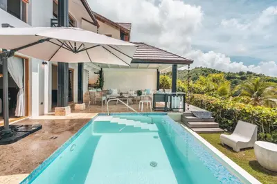 a swimming pool with an umbrella next to a house at Magnificent villa with ocean view in Puerto Bahia in Sabana
