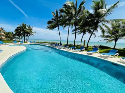 a swimming pool with chairs and palm trees and the ocean at Victorian Condominio in Cabarete