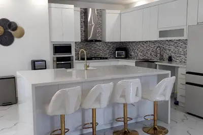 a kitchen with white cabinets and a counter with white stools at Bocachica house,apts,village in Jubey