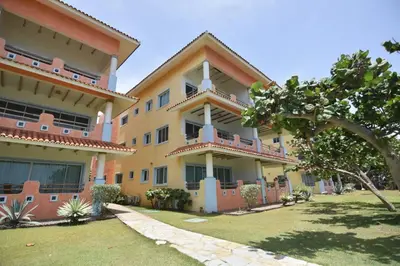 a large yellow building with a lawn in front of it at Bluefish Condo, Ocean Front, Sunrises, Pool, Hot Tub, Under New Management in Sosúa