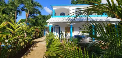 a blue and white house with palm trees and a fence at Charmant appartement cuisine 1 chambre AC Bonita in El Hoyo del Cacao