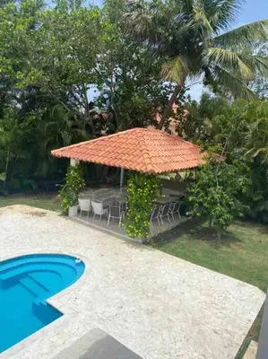a table with chairs and an umbrella next to a pool at Hermosa villa en metro country club Juan dolio in Paraíso