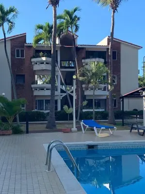 a swimming pool with palm trees and a building at Jungle Oasis by the Beach in San Felipe de Puerto Plata