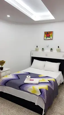 a white bedroom with a large bed with a purple and yellow blanket at Departamento en el centro in Santiago de los Caballeros