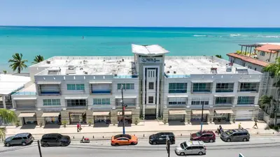 a large building with cars parked in front of the ocean at Beachfront Cabarete Apartment in Cabarete