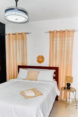 a bedroom with a bed with white sheets and a chandelier at Serene Beach Apartment in La Romana