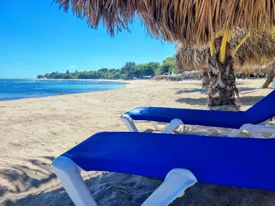 a blue beach chair sitting under a straw umbrella at Costambar Beachfront Stay with Pool in San Felipe de Puerto Plata