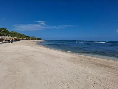 a sandy beach with umbrellas and the ocean at Costambar Seaside Apartment with Pool in San Felipe de Puerto Plata