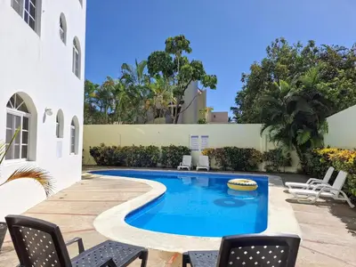 a swimming pool in a yard with chairs and a house at Costambar Seaside Apartment with Pool in San Felipe de Puerto Plata