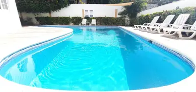 a swimming pool with chairs and a swimming pool at Cozy Apartment in Gated Community Costambar, Puerto Plata in San Felipe de Puerto Plata