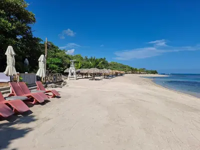 a beach with chairs and umbrellas and the ocean at Cozy Apartment in Gated Community Costambar, Puerto Plata in San Felipe de Puerto Plata