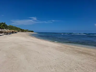 a sandy beach with umbrellas and the ocean at Cozy Apartment in Gated Community Costambar, Puerto Plata in San Felipe de Puerto Plata