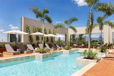 a pool with lounge chairs and umbrellas at a hotel at Hotel Santiago, Curio Collection By Hilton in Santiago de los Caballeros