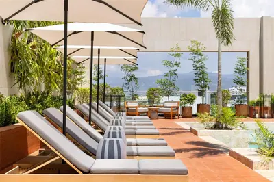 a row of lounge chairs with umbrellas on a building at Hotel Santiago, Curio Collection By Hilton in Santiago de los Caballeros