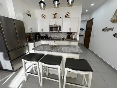 a kitchen with a island with two chairs and a refrigerator at Acogedor Apartamento en JUAN DOLIO in Los Corrales